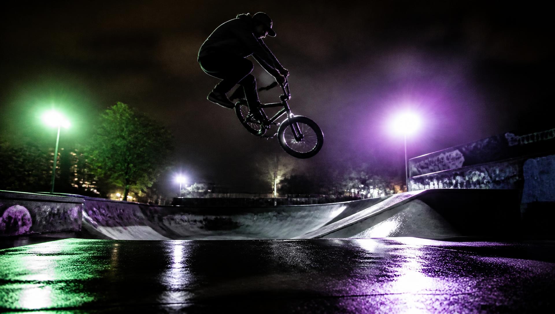 BMX rider în skatepark, noaptea, cu lumini neon verzi și mov